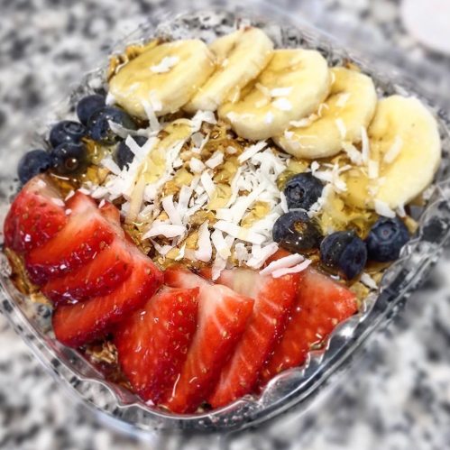 A colorful bowl of granola topped with sliced bananas, strawberries, blueberries, and shredded coconut.