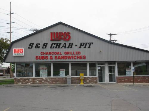 Exterior of Lupo's S&S Char-Pit, featuring a sign for charcoal grilled subs and sandwiches, with a parking lot in front.