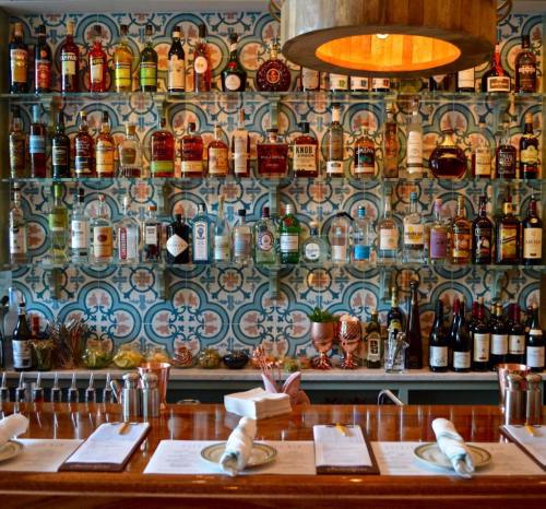 A stylish bar with a colorful tiled wall, showcasing various bottles of spirits and a polished wooden counter.