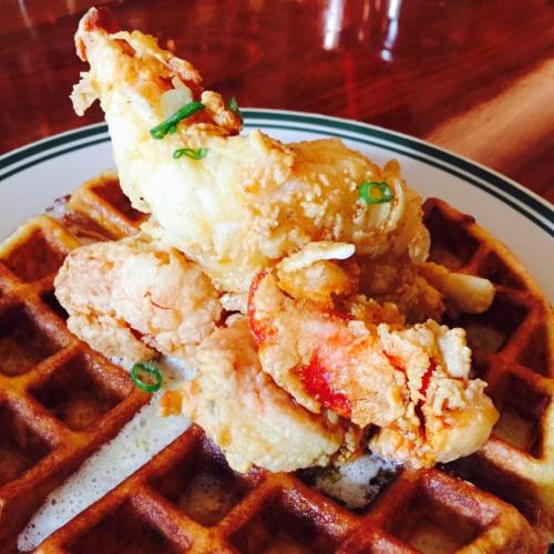 A plate of crispy fried chicken and shrimp served on a waffle, drizzled with syrup and garnished with green onions.