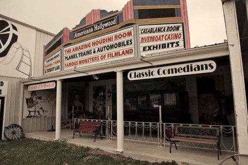 Exterior of a museum featuring signs for exhibits like the Houdini Room and Classic Comedians, with benches in front.