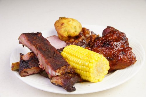 A plate of barbecue ribs, corn on the cob, baked beans, and a cornbread muffin.