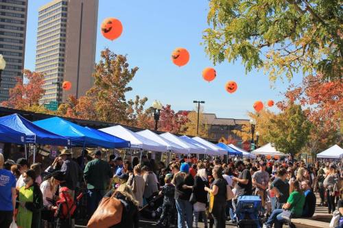A bustling outdoor market with colorful tents, autumn trees, and orange pumpkin decorations floating above.