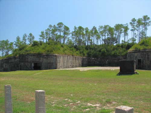 Abandoned concrete structure surrounded by green grass and trees under a clear blue sky.