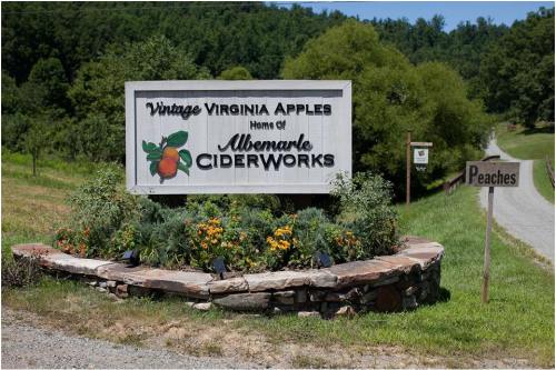 Sign for Vintage Virginia Apples, home of Albemarle Ciderworks, with a nearby sign pointing to peaches. Green landscape in background.