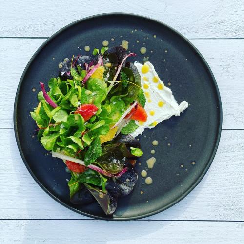 A vibrant salad with mixed greens, colorful vegetables, and a dollop of creamy cheese on a black plate.