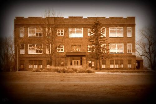 A vintage-style photo of a brick building with large windows, surrounded by grass and trees.