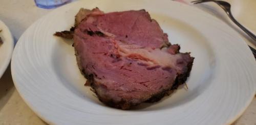 A thick slice of medium-rare prime rib on a white plate, showcasing its pink interior and crispy outer crust.
