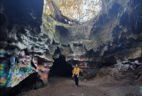 A person stands inside a colorful, rocky cave with natural light streaming in from above.