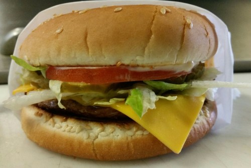 A sesame seed bun sandwich with lettuce, tomato, pickles, cheese, and a patty, topped with ketchup and mayonnaise.