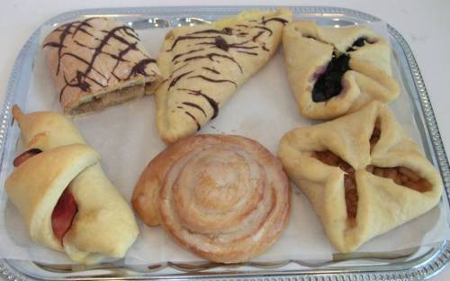 A tray of assorted pastries, including chocolate drizzled, fruit-filled, and cinnamon rolls, arranged neatly.