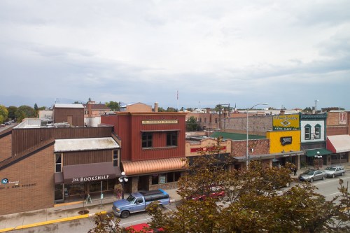 A view of a small town street featuring shops, restaurants, and cloudy skies in the background.