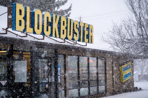 A Blockbuster store sign is visible in a heavy snowstorm, with snowflakes falling around the entrance.