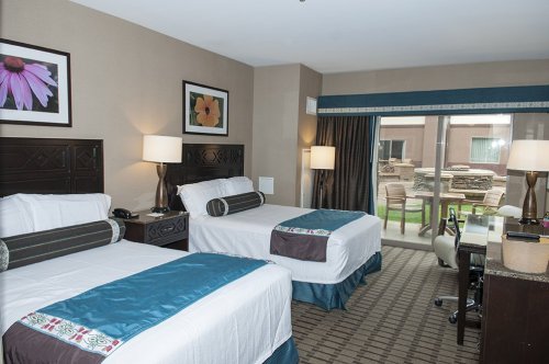 A hotel room with two beds, decorative pillows, a desk, and a view of an outdoor area through sliding glass doors.