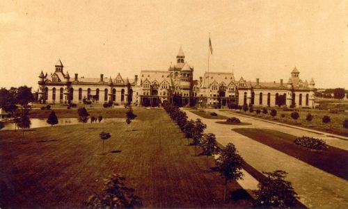 Historic building with ornate architecture, surrounded by manicured lawns and trees, captured in sepia tones.