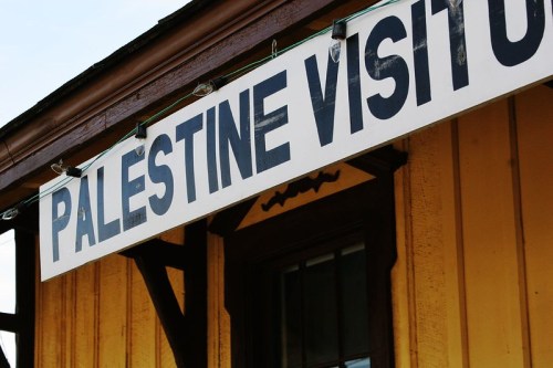 Sign reading "Palestine Visitor" on a yellow building with wooden beams.