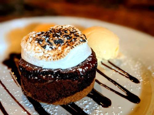 A chocolate dessert with a toasted meringue topping, served with a scoop of vanilla ice cream and drizzled with chocolate sauce.