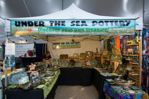 A pottery booth with a sign reading "Under the Sea Pottery," showcasing various ceramic pieces and a vendor in the background.