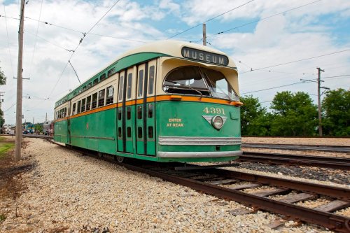 A vintage green and cream streetcar labeled "MUSEUM" parked on tracks with a cloudy sky in the background.