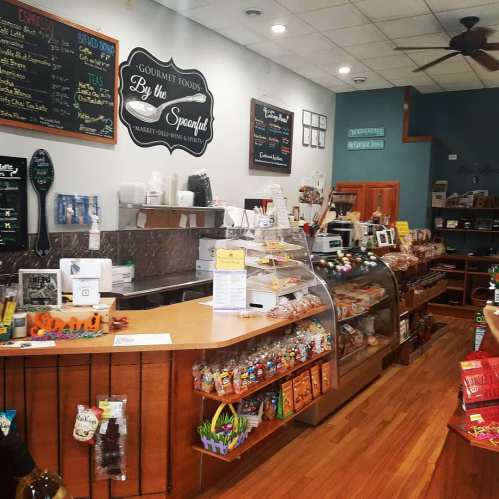 A cozy gourmet food shop interior featuring a display counter, shelves of snacks, and a chalkboard menu.