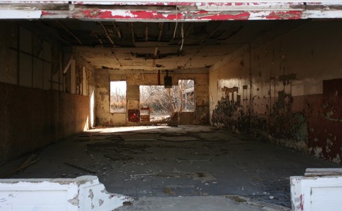 An abandoned, dilapidated interior with peeling paint and debris, illuminated by natural light from broken windows.