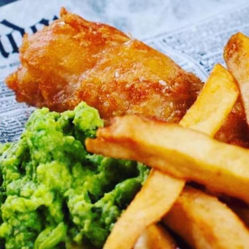 A plate featuring crispy fried fish, golden fries, and vibrant green mushy peas on a newspaper backdrop.