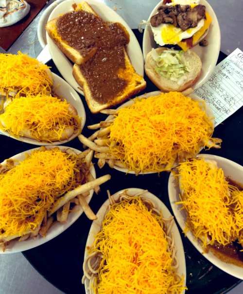 A tray of food featuring several bowls of chili cheese fries and a sandwich with toppings.
