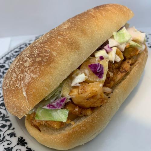 A freshly made sandwich in a crusty roll, filled with shredded chicken and colorful vegetables.