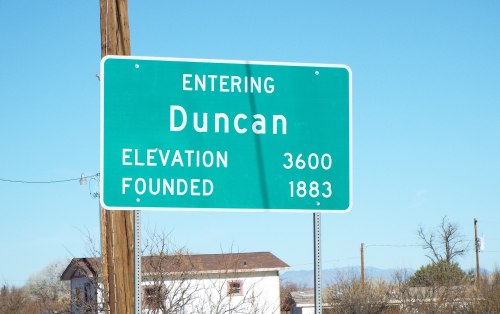 Green road sign indicating "Entering Duncan," with elevation 3600 and founded in 1883. Clear blue sky in the background.