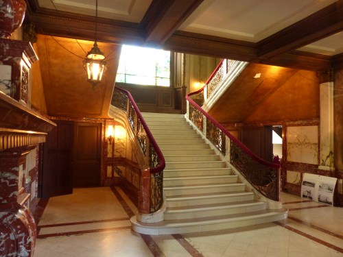 Elegant interior featuring a grand staircase, ornate railings, and stained glass windows in a richly decorated space.