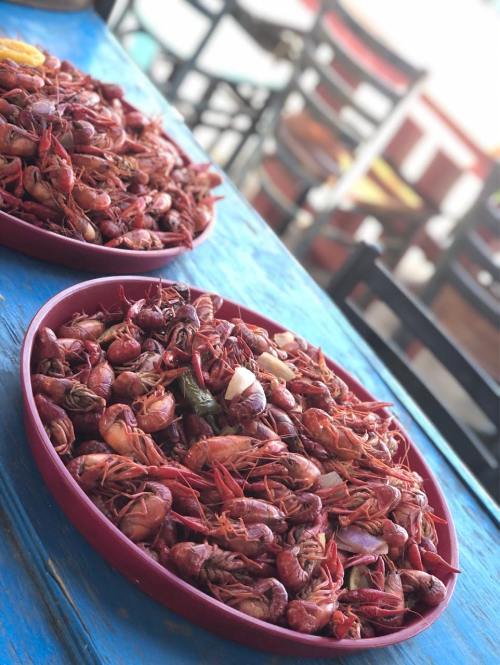 Two large red trays filled with cooked crawfish, set on a blue table with chairs in the background.
