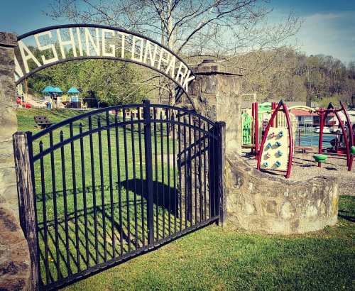 A black gate with "Washing Park" sign opens to a playground with climbing structures and green grass in the background.