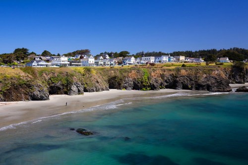 Coastal view of a beach with rocky cliffs and a charming town in the background under a clear blue sky.