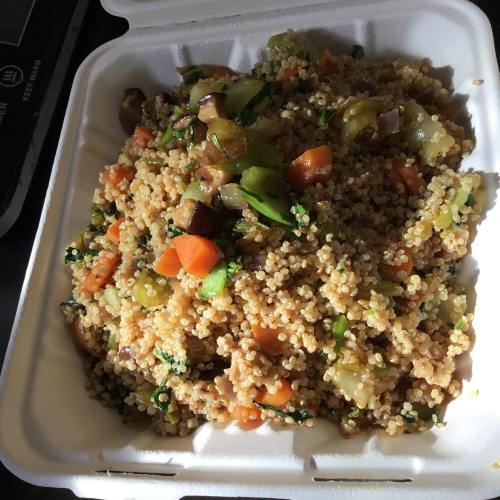 A close-up of a colorful quinoa dish with mixed vegetables in a takeout container.