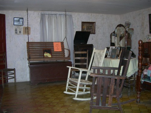 A cozy room with vintage furniture, including rocking chairs, a wooden bench, and framed photos on the walls.