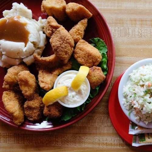 A plate of fried chicken pieces with mashed potatoes, gravy, coleslaw, and a dipping sauce with lemon wedges.
