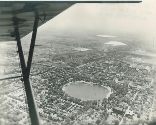 Aerial view of a city with a circular lake surrounded by buildings and greenery, captured from an airplane.