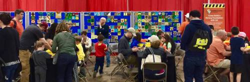 A busy community event with families and children engaged in activities at tables, surrounded by colorful artwork displays.