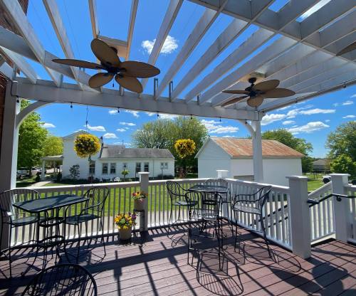 A sunny outdoor patio with ceiling fans, tables, and chairs, overlooking a green lawn and white buildings.