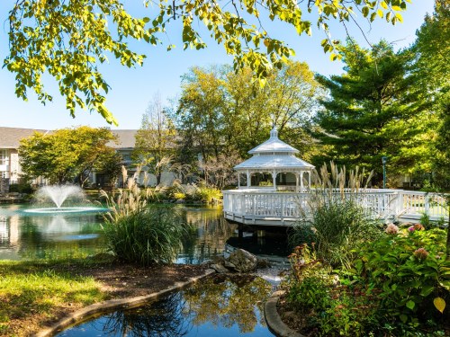 A serene garden scene featuring a gazebo by a pond, surrounded by lush greenery and a fountain.
