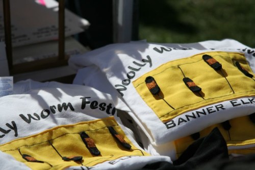 Two white t-shirts featuring a yellow design with the text "Woolly Worm Festival" and "Banner Elk."