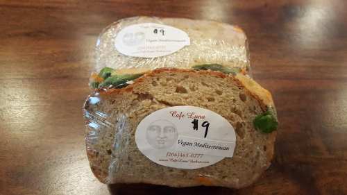 Two wrapped vegan Mediterranean sandwiches with price tags on a wooden table.