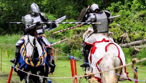 Two armored knights on horseback engage in a jousting match, with lances raised in a grassy arena.