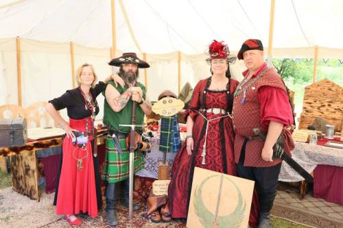 A group of four people in medieval costumes pose inside a tent, showcasing their attire and accessories.