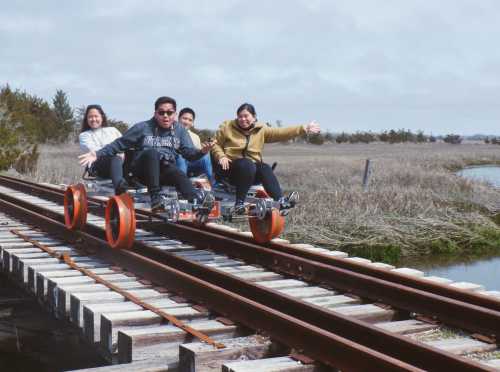 A group of five people joyfully riding on a rail bike along a wooden railway track in a scenic outdoor setting.