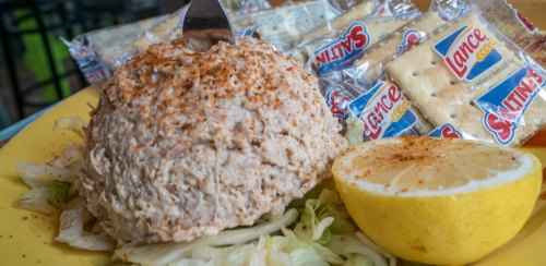 A plate featuring a large tuna salad ball, crackers, and a lemon wedge, garnished with spices and served on lettuce.