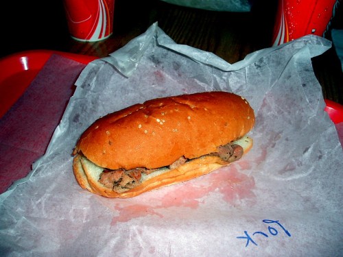 A sesame seed bun filled with sliced meat, resting on a piece of parchment paper, with a red tray in the background.