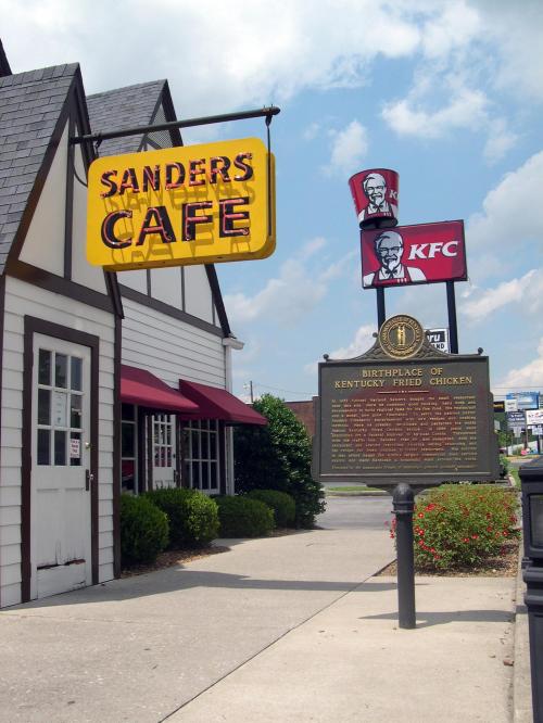 Sign for Sanders Cafe with KFC logo and a historical marker about the birthplace of Kentucky Fried Chicken.
