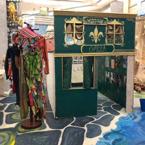 A colorful miniature theater set with a green façade labeled "Opéra" and a display of costumes nearby.