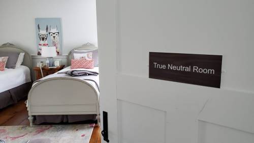 A doorway leading to a room labeled "True Neutral Room," featuring two beds and decorative artwork.
